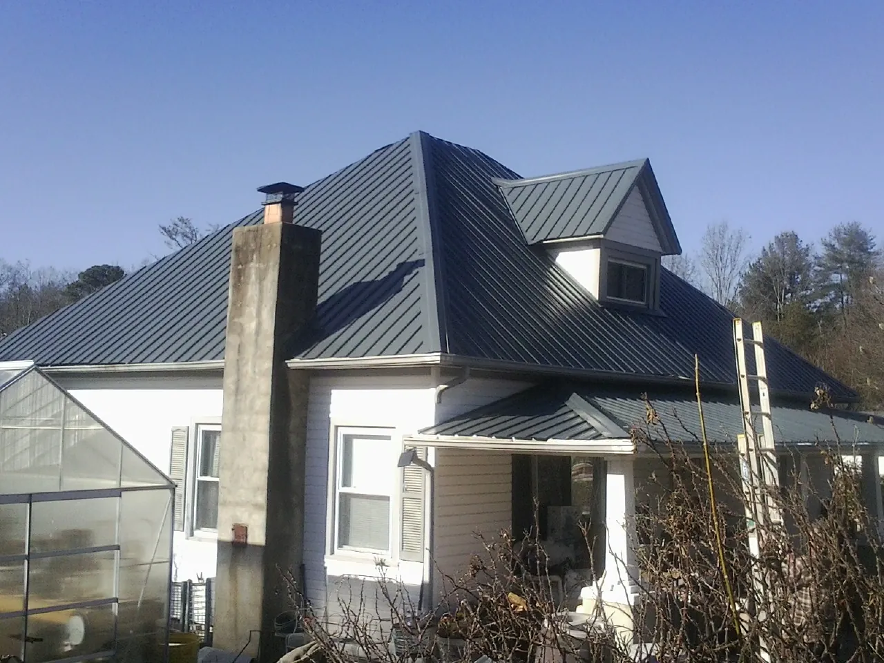 Dark blue standing seam metal roof on a white farmhouse with dormer — Slate & Tile Roof Repair by Roofing Brothers in Magazine