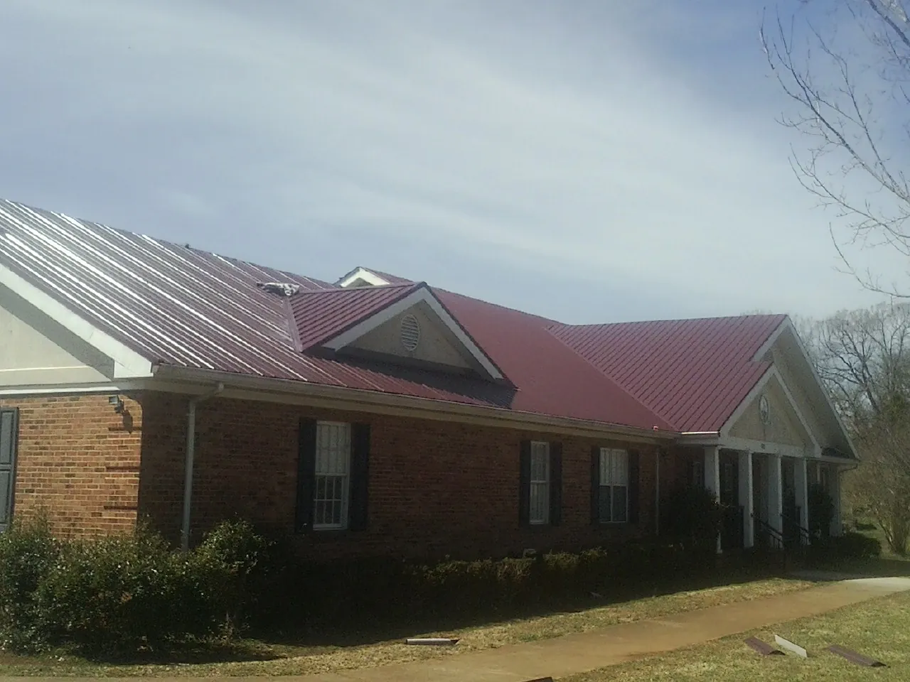 Red metal roof with gabled entries on a long brick building, from a Hail Damage Roof Repair job in Magazine