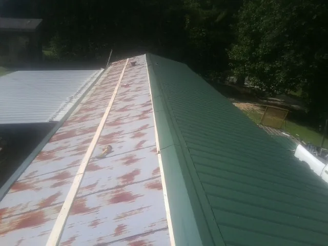 Old rusted panels beside newly installed green metal roofing — Wind Damage Roof Repair by Roofing Brothers in Magazine