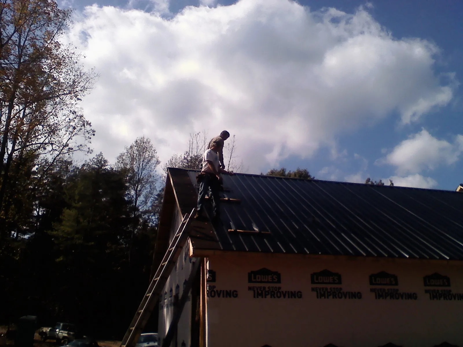 Roofer fastening dark metal panels high against a cloudy sky, from a Roof Inspection job in Magazine