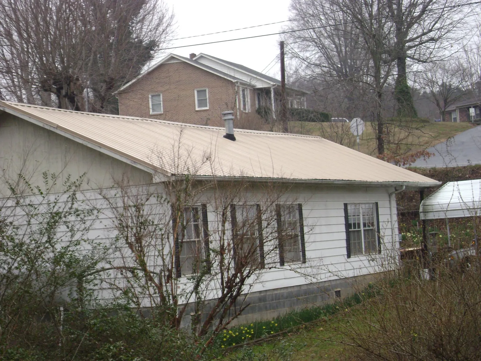 Tan metal roof on a white sided house set into a hillside — Commercial Roofing by Roofing Brothers in Magazine