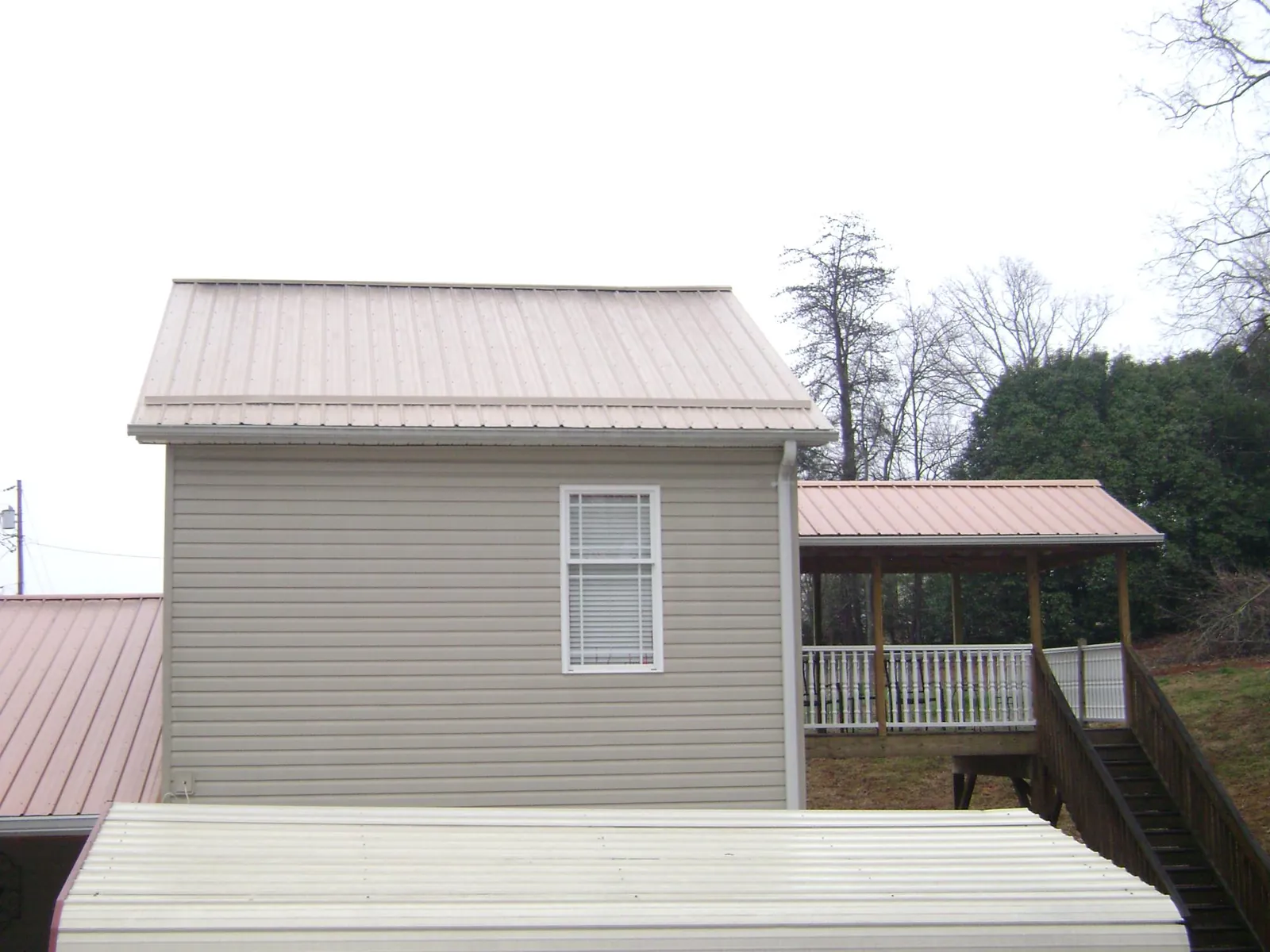 Tan metal roofs on a two story addition and attached porch, from a Roof Replacement job in Magazine